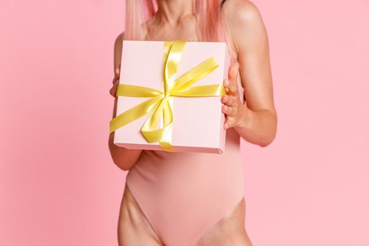 Close up shot of woman in swimsuit holding cute gift box, standing isolated over pink background. Holiday, birthday concept