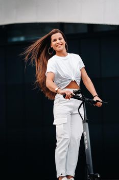 beautiful girl in white stylish clothes on an electric scooter in the city.