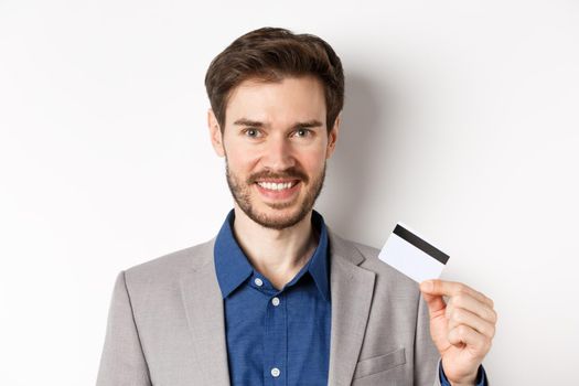Shopping. Handsome candid business man in suit showing plastic credit card and smiling, recommending bank, white background.