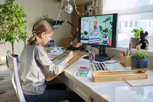 Creative online drawing lesson. Girl child drawing with watercolors, looking at computer monitor, talking with the teacher young artist