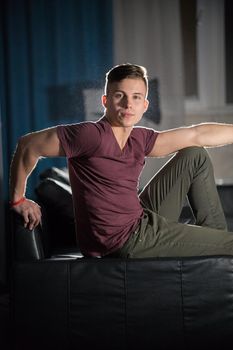 Young attractive fit guy posing for the camera. Sitting on a couch, looking in the camera. Portrait