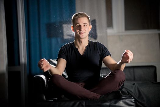 Young attractive smiling guy sitting in lotus pose. Portrait
