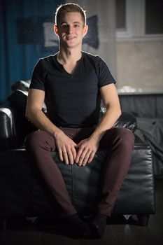 Young attractive smiling guy in dark t-shirt sitting on a couch. Portrait