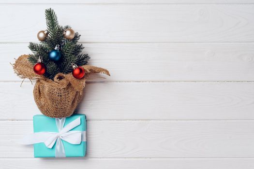 Pine tree decorated with baubles and wrapped Christmas gifts on white wooden background top view