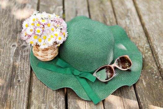 daisies lying on a green hat near sunglasses. Designer old-fashioned floristics bouquet of meadow and wild flowers. A romantic photo of a cute spring bouquet. hat with bouquet of daisies. summer vacation concept