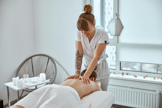 Professional confident massage master is doing procedures to caucasian woman in minimalistic modern cabinet