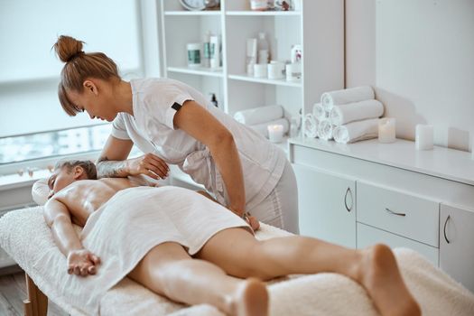 Professional confident massage master is doing procedures to caucasian woman in minimalistic modern cabinet