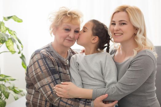 Portrait of three generations of women look at camera posing for family picture, cute little girl hug mom and granny enjoy time at home, smiling mother, daughter and grandmother spend weekend together