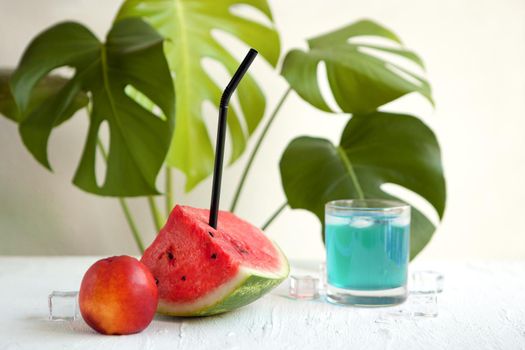 watermelon and blue curacao cocktail on the white board. Delicious cocktail drink with fresh fruits with peach and ice. watermelon blue summer cocktail infront of monstera tropical plant