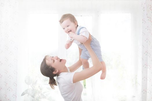 Young mother holding her newborn child. Mom nursing baby. Woman and new born boy relax in a white bedroom. Nursery interior. Mother breast feeding baby. Family at home