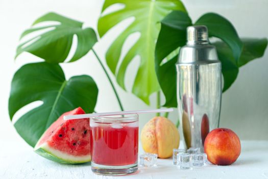 watermelon smoothie on the white board. Delicious Smoothie - vegetarian coctail from fresh fruit with peach and ice. watermelon summer cocktail infront of monstera tropical plant