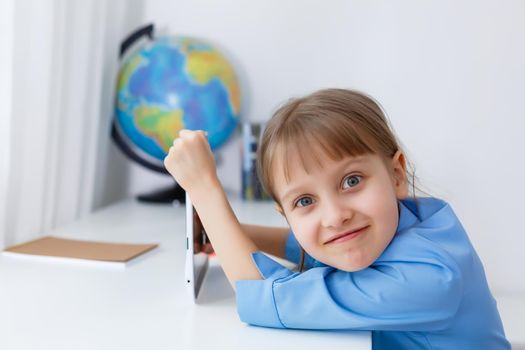 Cute little girl is sitting at table with her laptop and studying online