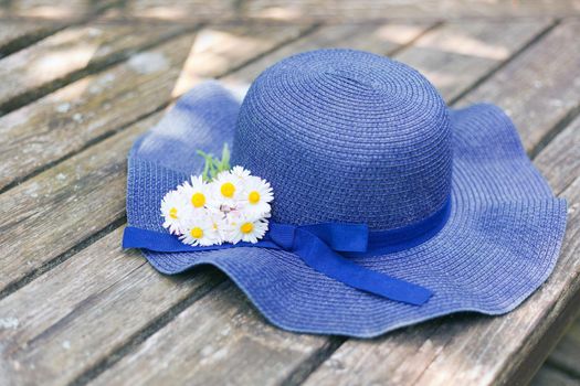 blue hat lying on a wooden bench with small daisies bouquet at sunny day. bouquet of meadow and wild flowers. romantic photo of a cute summer time. vacation concept