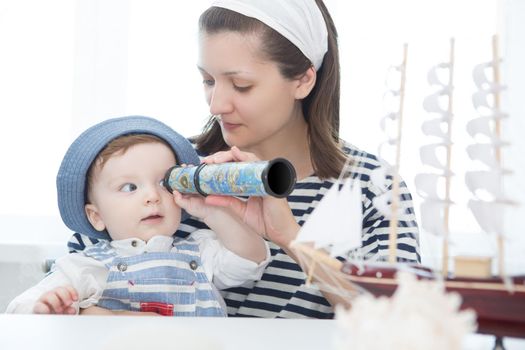 Happy kid and mom playing with toy sailing boat indoors. Travel and adventure concept