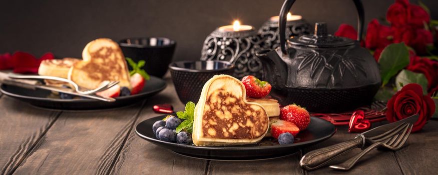 Valentine's day greeting card with delicious pancakes in form of heart, green tea, black teapot, candles and roses. Valentines day concept. Copy space. Banner.