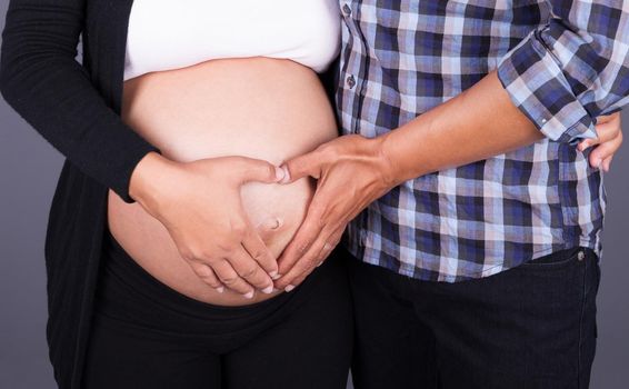 close up hands of couple making a heart shape on the woman's pregnant belly