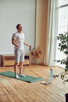 Guy is doing training with equipment in front of notebook and bottle of water during quarantine