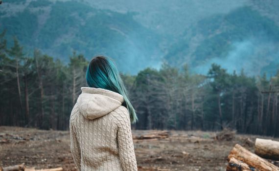Unrecognizable young woman with blue hair looking at the forest, rear view