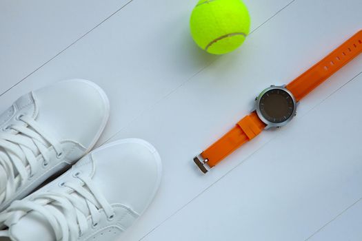 white tennis shoes, tennis ball and orange sport watch. sportequipment. sportswear. Participation in competition.