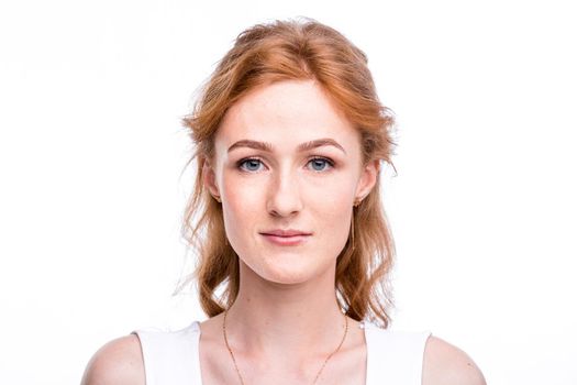 Portrait of a beautiful young woman of European, Caucasian nationality with long red hair and freckles on her face posing on a white background in the studio. Close-up student girl in a white blouse.