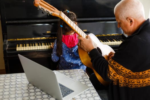 little girl plays piano together with grandfather, learning online on a laptop