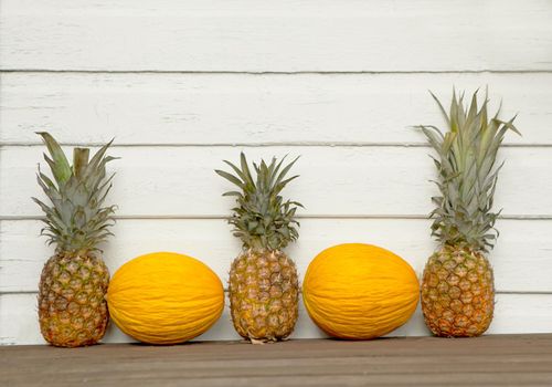 Melons and Pineapple behind the white wooden-timber background. Funny summer Wallpaper. fruit decorations