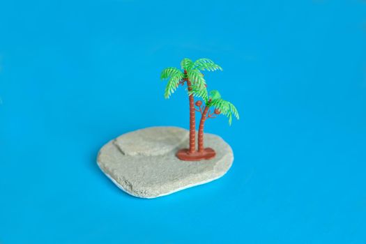 toy palmtree on the stone at blue paper. Minimalistic image plastic toys at the beach. vacation concept