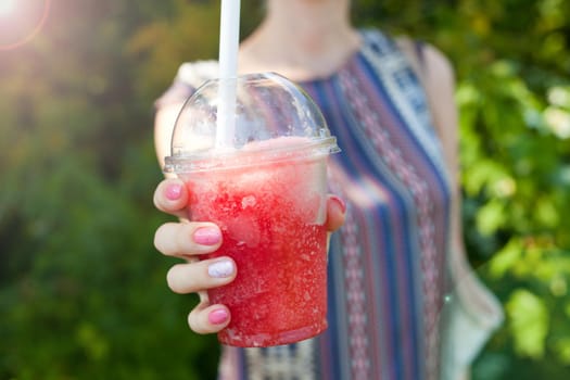 woman Hand holding Red Ice water in plastic cup. Ice beverage - cold healthy summer drink or cocktail. sunny day