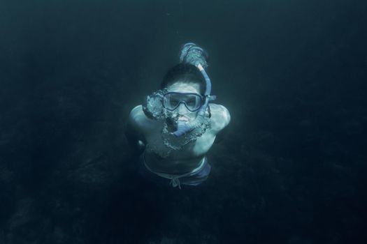 Young man in mask and snorkel swimming underwater in deep sea.