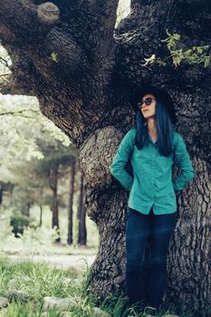 Casual style young woman with blue hair standing near the oak tree in spring