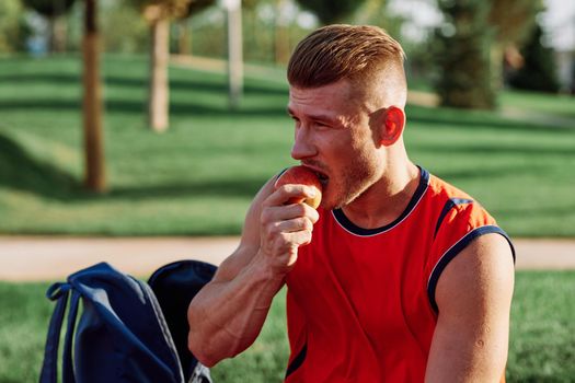 man in the park sits on a bench and eats an apple summer. High quality photo