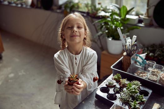 Young happy caucasian kid girl is holding a plant in her hands at botanic store