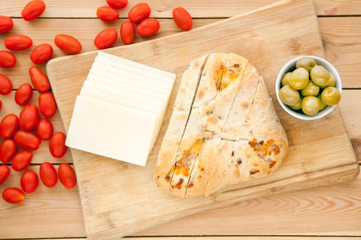 Fresh whole grain bread with cheese and green olives and tomatoes. Natural food concept. Loaf of organic bread on wooden background.