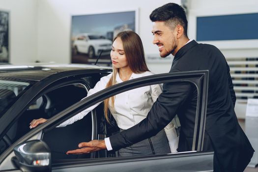 Man car dealer showing a woman buyer a new car in car salon
