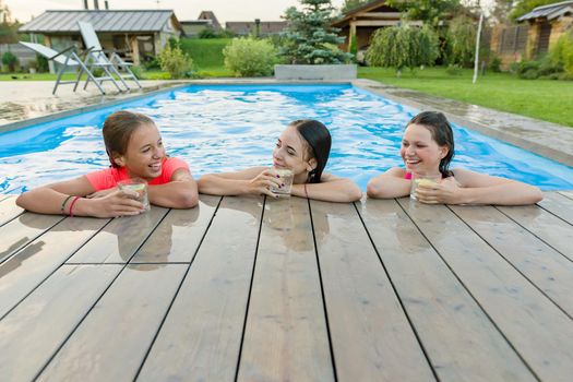 Three happy girls with beverages on summer party in the swimming pool