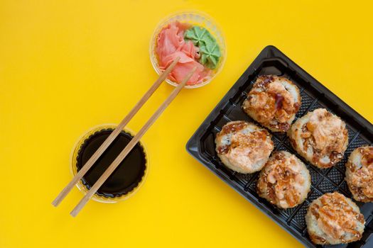 flat lay set with ginger and wasabi - baked sushi set with salmon in plastic packaging on yellow background - bright delicious set of sushi rolls