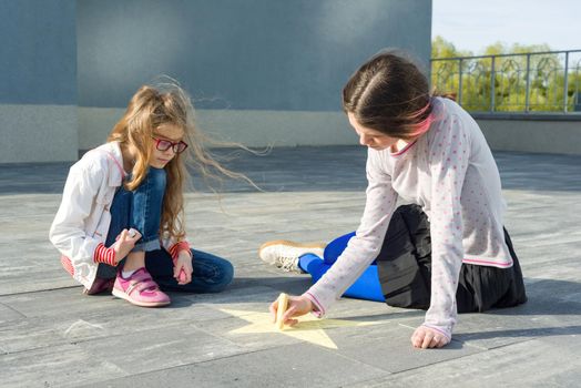 Children, girls draw on the asphalt colored crayons symbol - star.