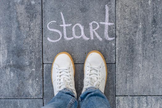 Female legs shod in white sneakers and the word start