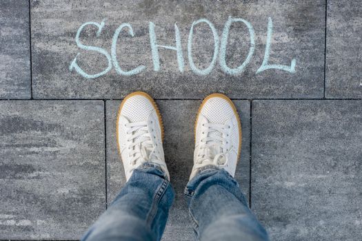The word school on the asphalt and the feet of the student. Back to school!