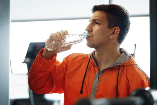 Portrait of young man drinking some water from a bottle in a gym, close up