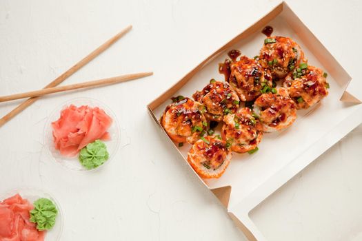 flat lay set with ginger and wasabi - baked sushi set with salmon in paper packaging on white background - bright delicious set of sushi rolls