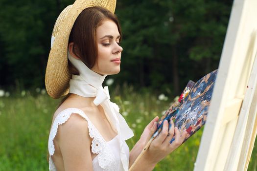 pretty woman in hat artist paints a picture on nature paint. High quality photo