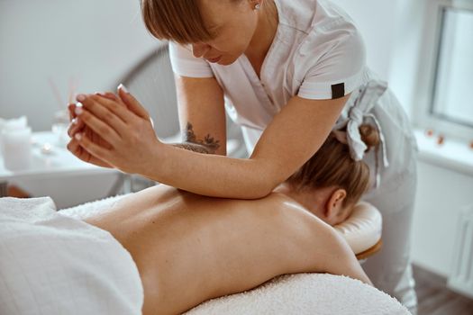 Professional confident massage master is doing procedures to caucasian woman in minimalistic modern cabinet