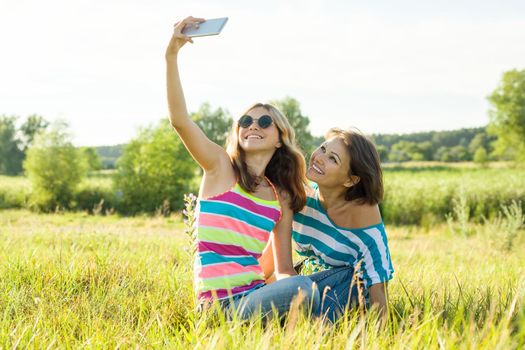 Communication between the mother and the teen daughter. Photos on a smartphone together. Nature sunset background.