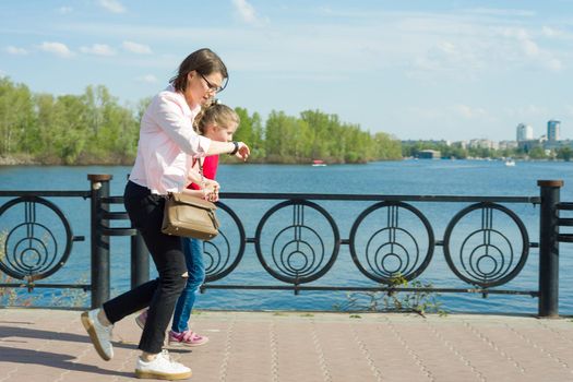 Mother and little daughter go to school. Woman looks at her watch, hurries, is late, quickly goes.