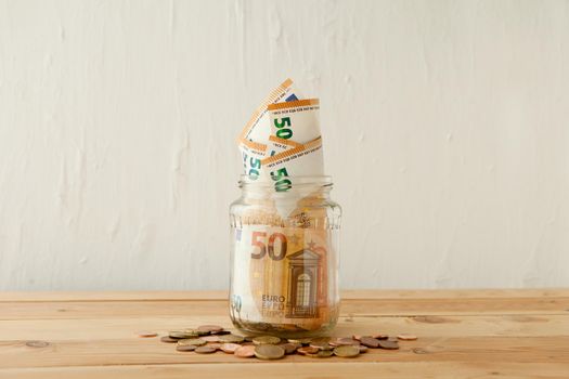 euro money banknotes in the glass jar at wooden table with euro coins or cents. Business concept. Money cash savings in glass pot at home.