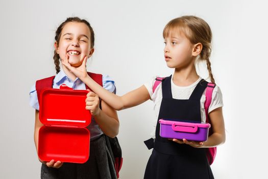 Pupils of primary school with lunch-boxes in hands. Girls with backpacks are eating fruit. Beginning of lessons. First day of fall.