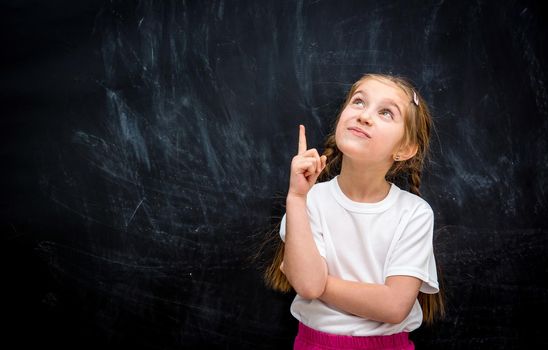 Cute little girl looking up with the idea on a background of black school board