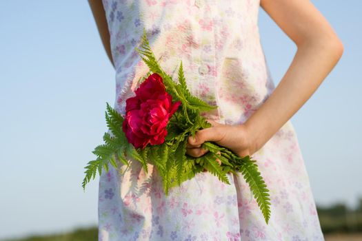 Little child girl holding bouquet of flowers. A bouquet behind your back.