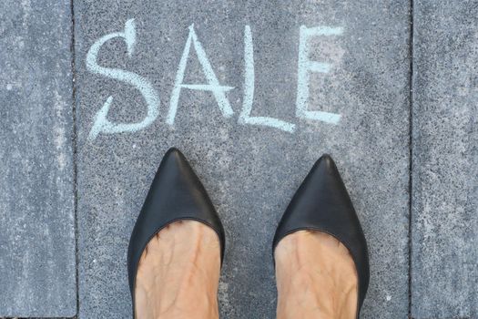 Sale ahead concept with woman feet on asphalt road with text